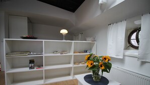 Una habitación con estanterías blancas, una pequeña mesa con un jarrón de girasoles y una ventana que ofrece vistas al exterior.