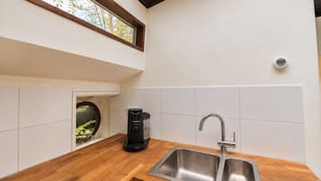 Una cocina moderna con cafetera integrada, un lavamanos doble y un ventanal con vistas a árboles.