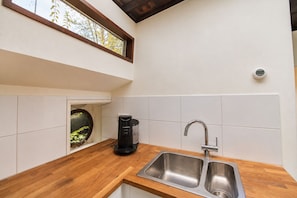 A modern kitchen with a built-in coffee maker, a double sink, and a window with a view of trees.