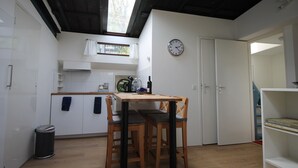 Cocina compacta con una mesa y sillas de madera, un reloj en la pared y vistas al exterior a través de un tragaluz.