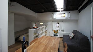 Un espacio habitable pequeño con una mesa de madera, un sofá, una cama y un tragaluz.
