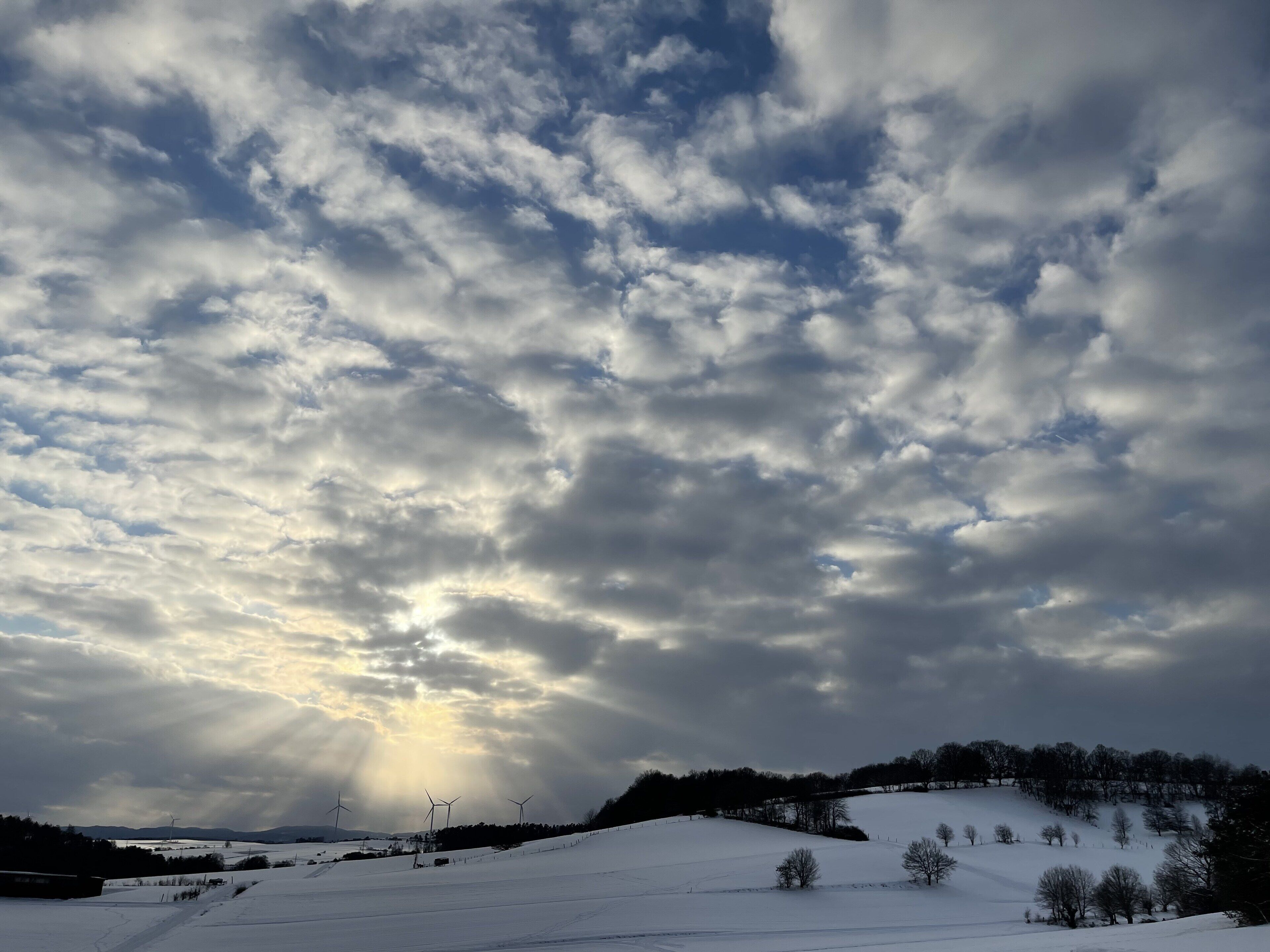 Schneebedeckte Landschaft mit Windkraftanlagen und einem bewölkten Himmel.