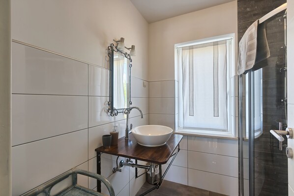 Une salle de bain moderne avec un grand lavabo blanc, un meuble-lavabo avec un miroir et une cabine de douche en verre.