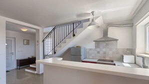 A modern kitchen with a white countertop, stainless steel appliances, and a staircase leading to another level. - Villa Pascal (Peruški)