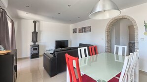 A modern living room with a fireplace, black sofa, TV, and a dining area with a glass table and red chairs. - Villa Pascal (Peruški)