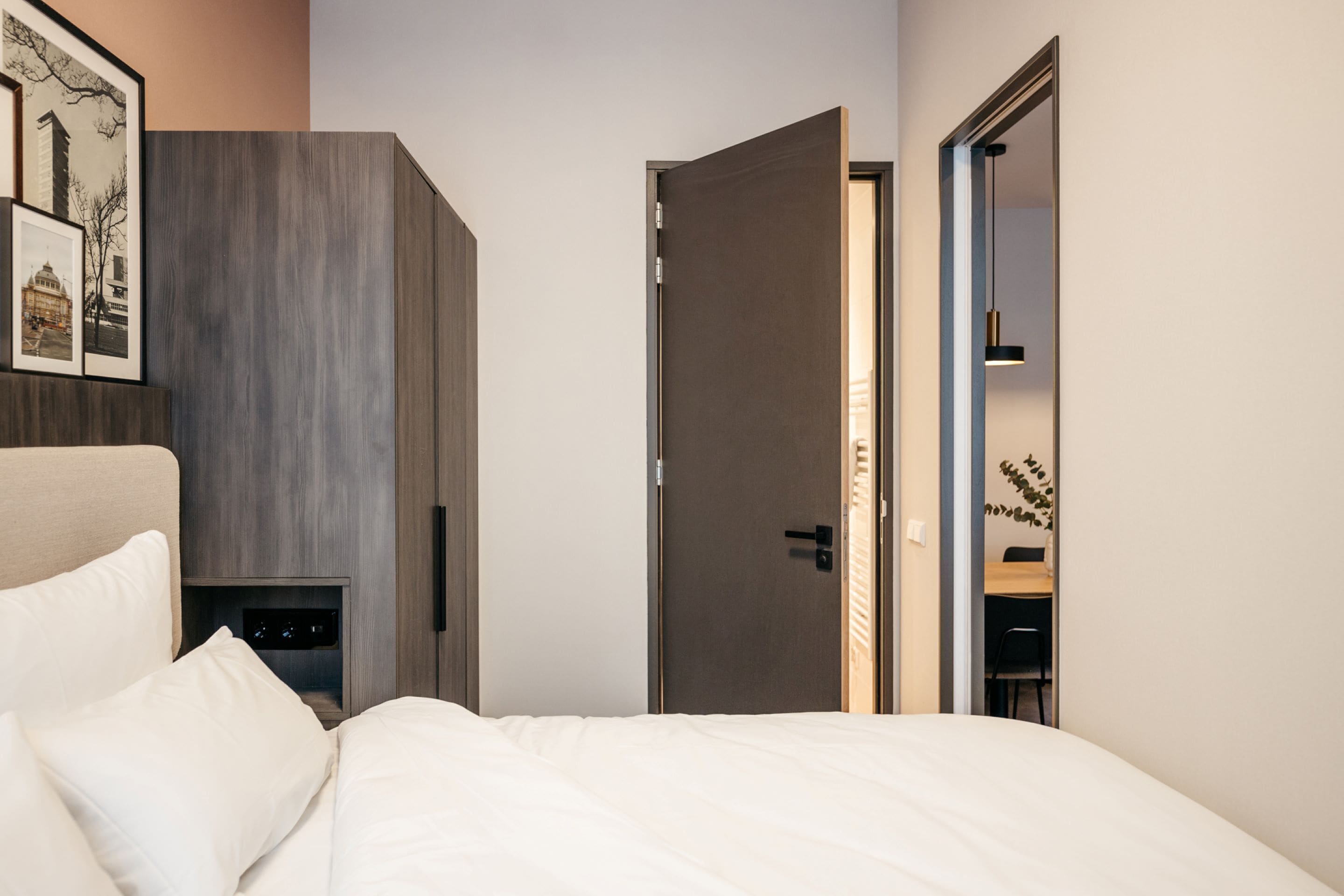Un dormitorio moderno con cama, mesita de noche, armario y puerta que da a otra habitación.