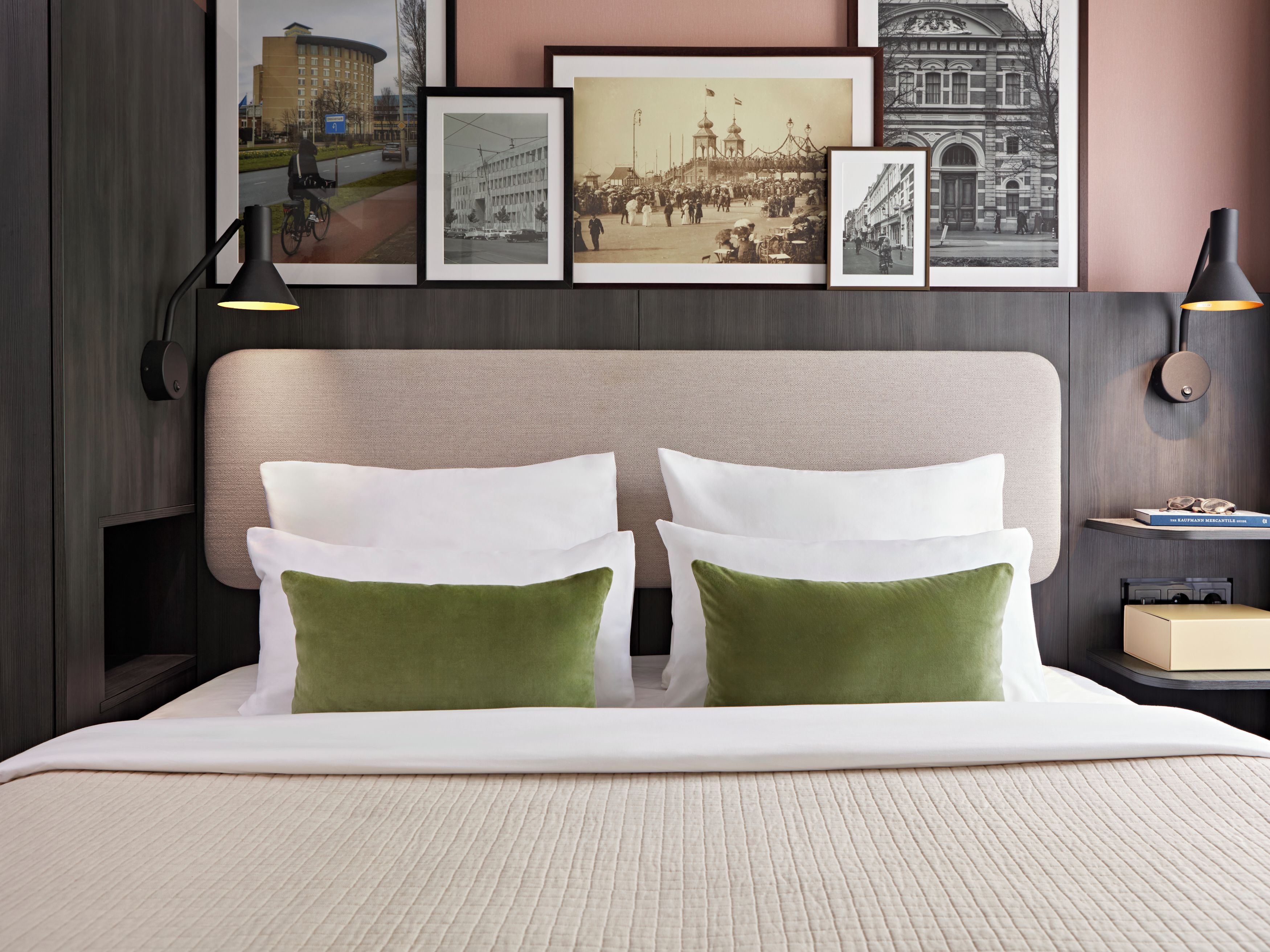Een hotelkamer met een bed, foto's aan de muur en een nachtkastje met een lamp.