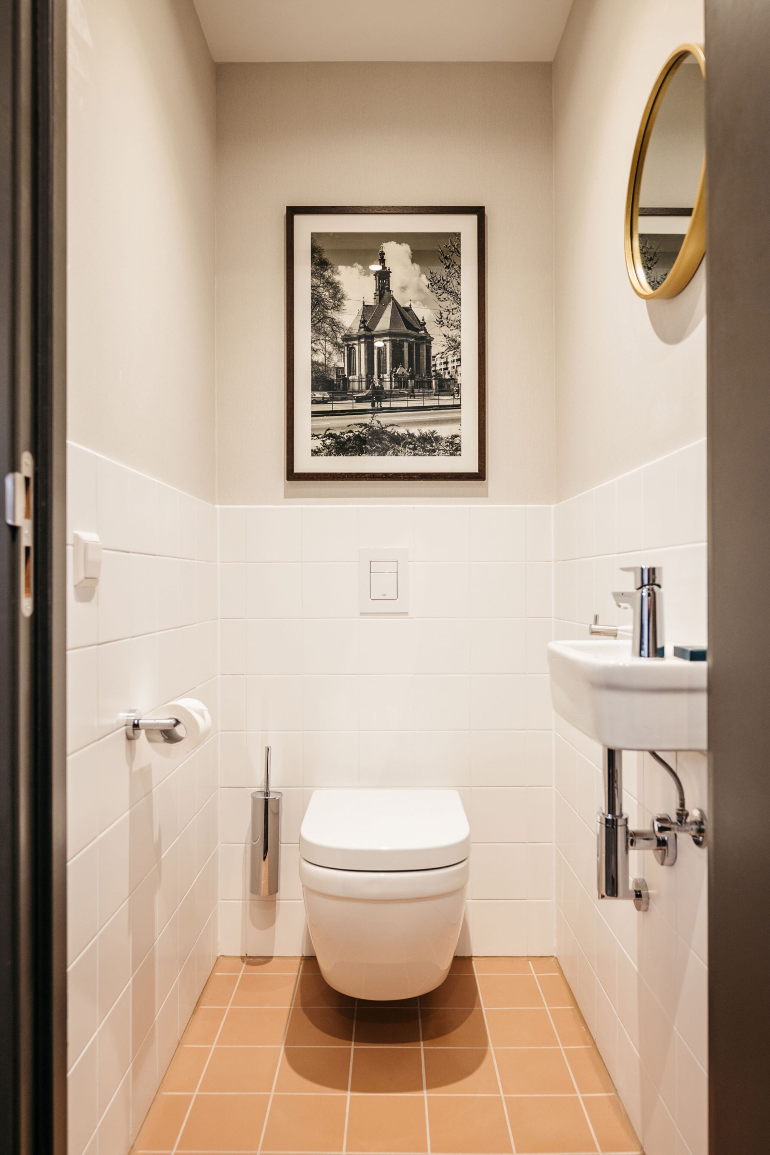 Ein kleines, sauberes Badezimmer mit weißen Fliesen, einer weißen Toilette, einem Waschbecken und einem gerahmten Bild an der Wand.