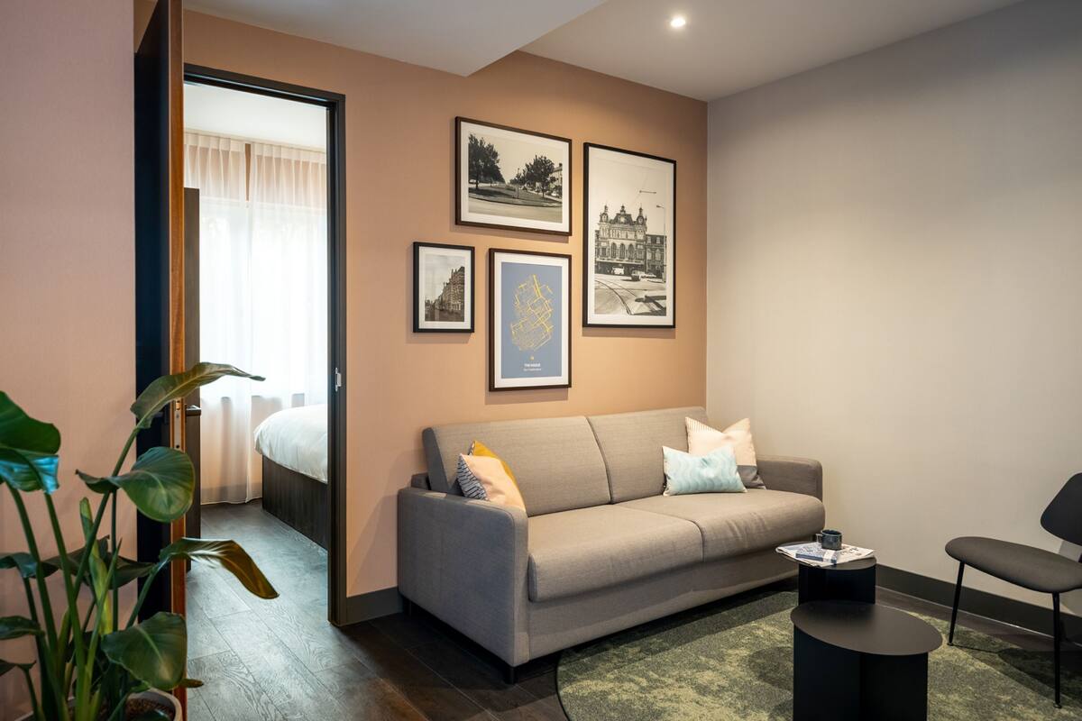 Un salon moderne avec un canapé, une table basse et un fauteuil. Des tableaux encadrés ornent le mur et une plante est placée dans un coin.