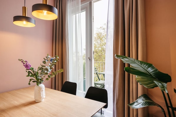 A dining area with a wooden table, two pendant lights, a vase with flowers, and a large plant.