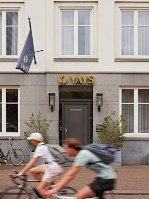 Un bâtiment avec une enseigne indiquant « YAYS » et un drapeau orné d’un logo. On y voit des fenêtres et une porte, et un vélo est garé à l’extérieur.