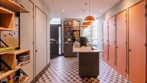 Een hotel lobby met een geruit vloertapijt, houten schappen, een centraal eiland met een laptop, en oranje lockers.