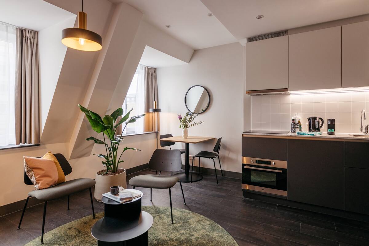 Une cuisine moderne avec un plancher en bois foncé, un coin repas avec une table et des chaises, et un espace détente avec un banc et une plante en pot.