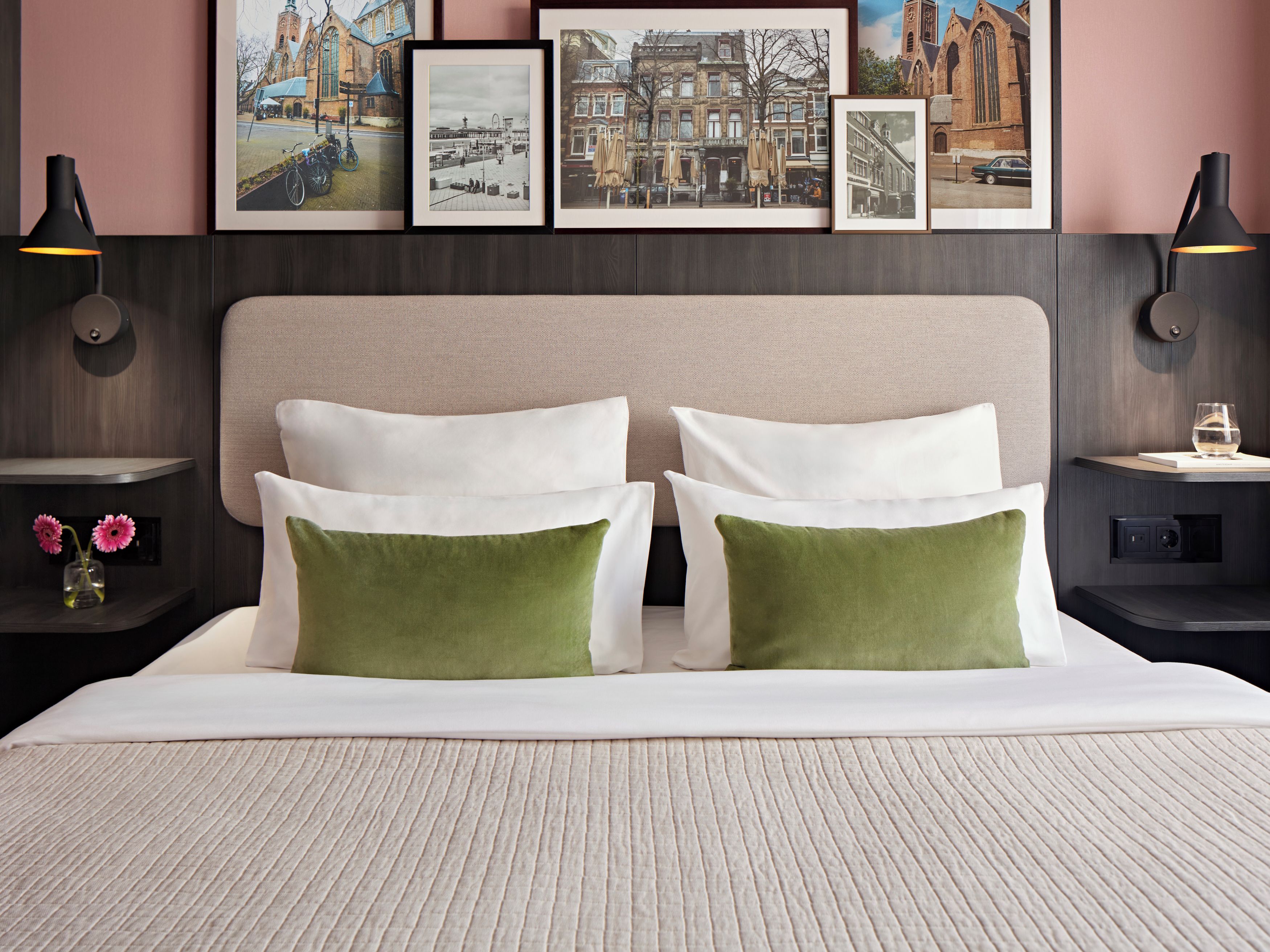 A neatly made bed with two pillows, a headboard, and a framed cityscape above.