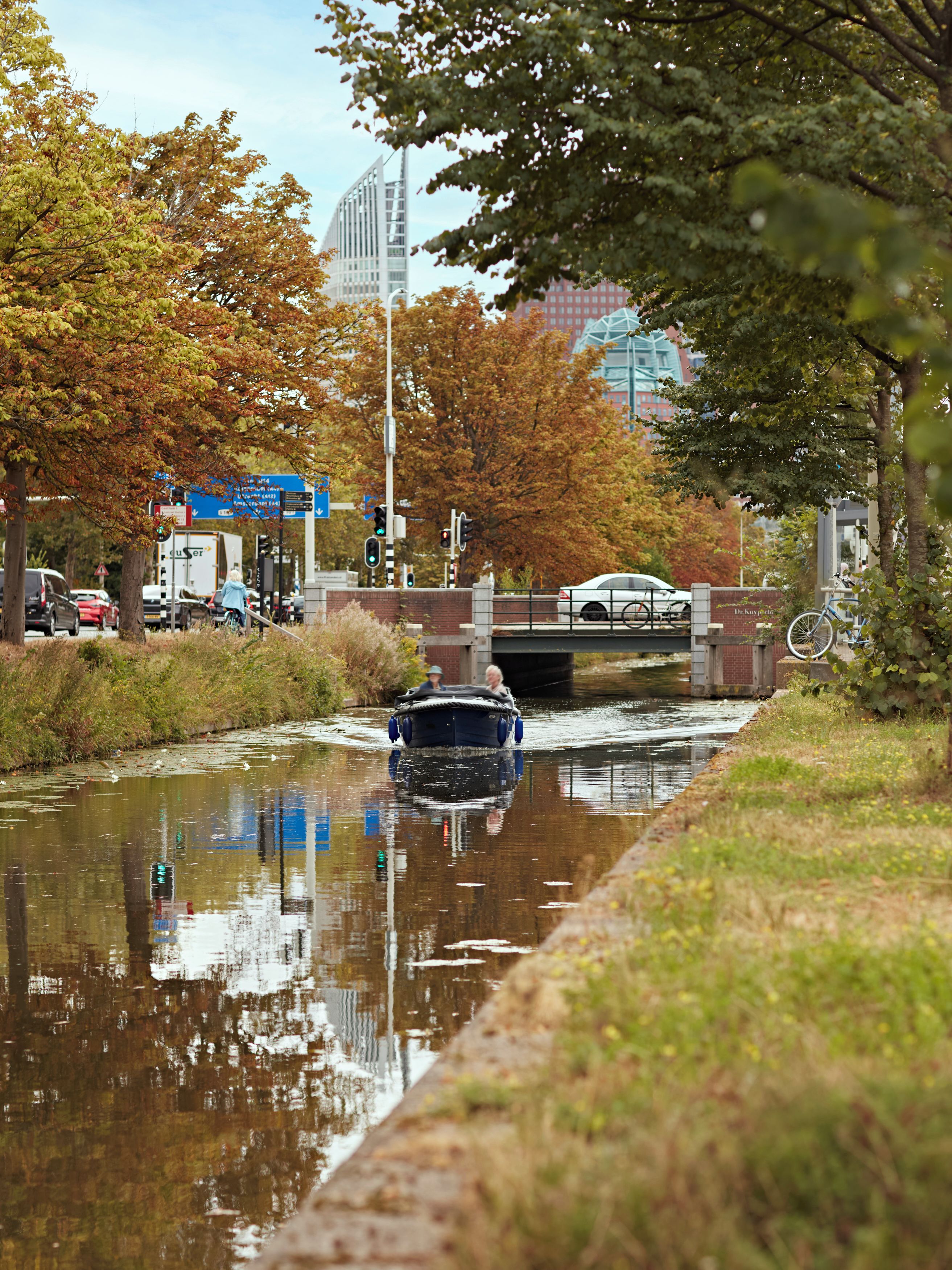 Un canal con un bote, árboles y un puente al fondo.