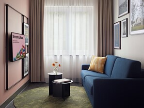 Un salon moderne avec un canapé bleu, une petite table d’appoint sur laquelle repose un livre, et un panneau d’accueil encadré.