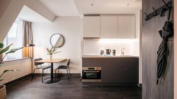 A modern kitchen with dark wood flooring, a dining area with a round table and chairs, and a large window providing natural light.