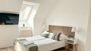 A modern bedroom with a sloped ceiling, a bed with white linens, a bedside table with a lamp, and a small plant on the windowsill. - Modern Apartment in The Heart of Vienna 9 (Vienna)