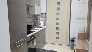 A compact kitchen with a stove, oven, and sink. There is a door with a frosted glass panel and a small wooden table with a trash bin. - Modern Apartment Vienna Congress Center (Vienna)