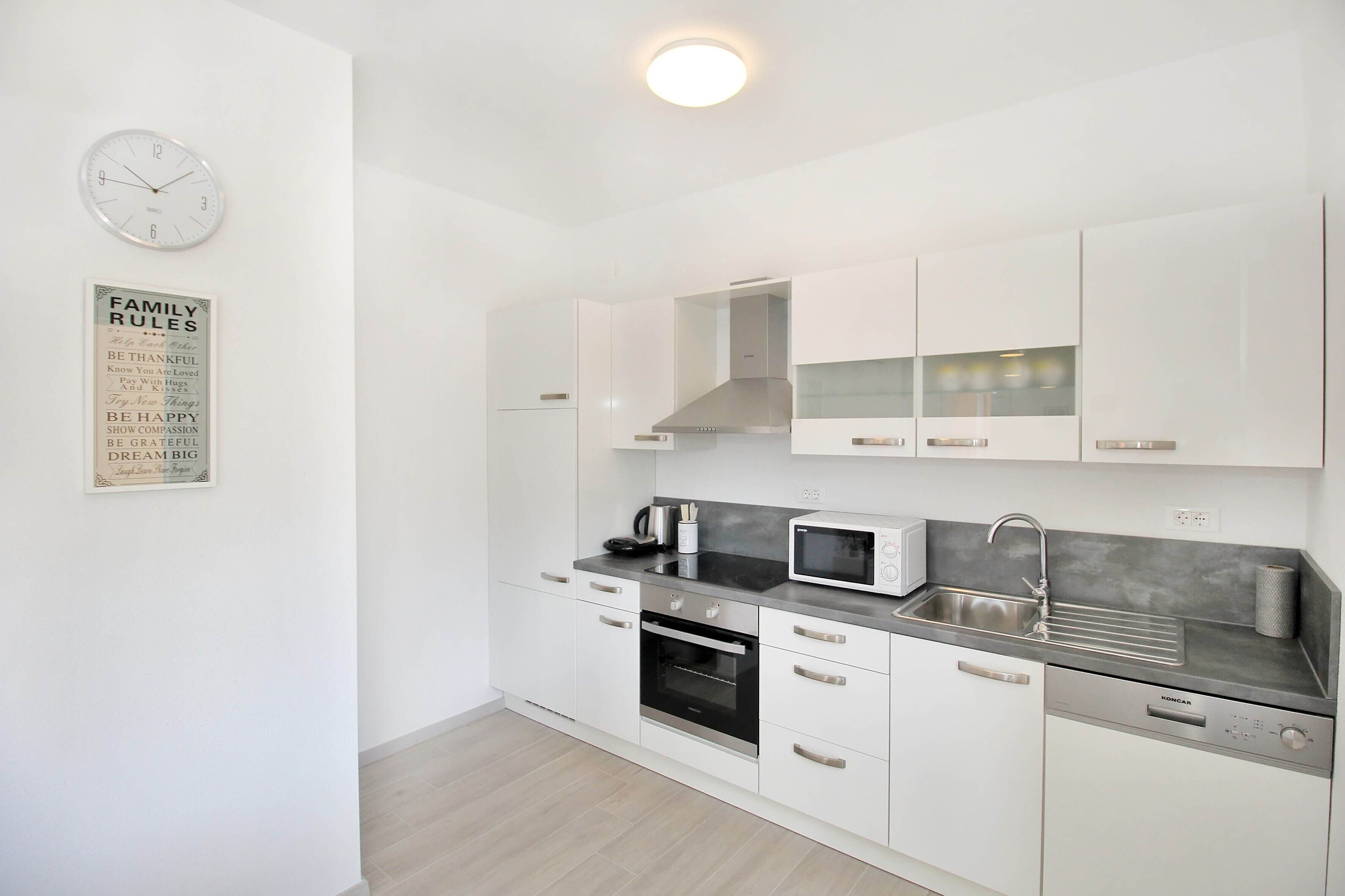 A modern kitchen with white cabinets, a built-in oven, a microwave, and a stainless steel sink.