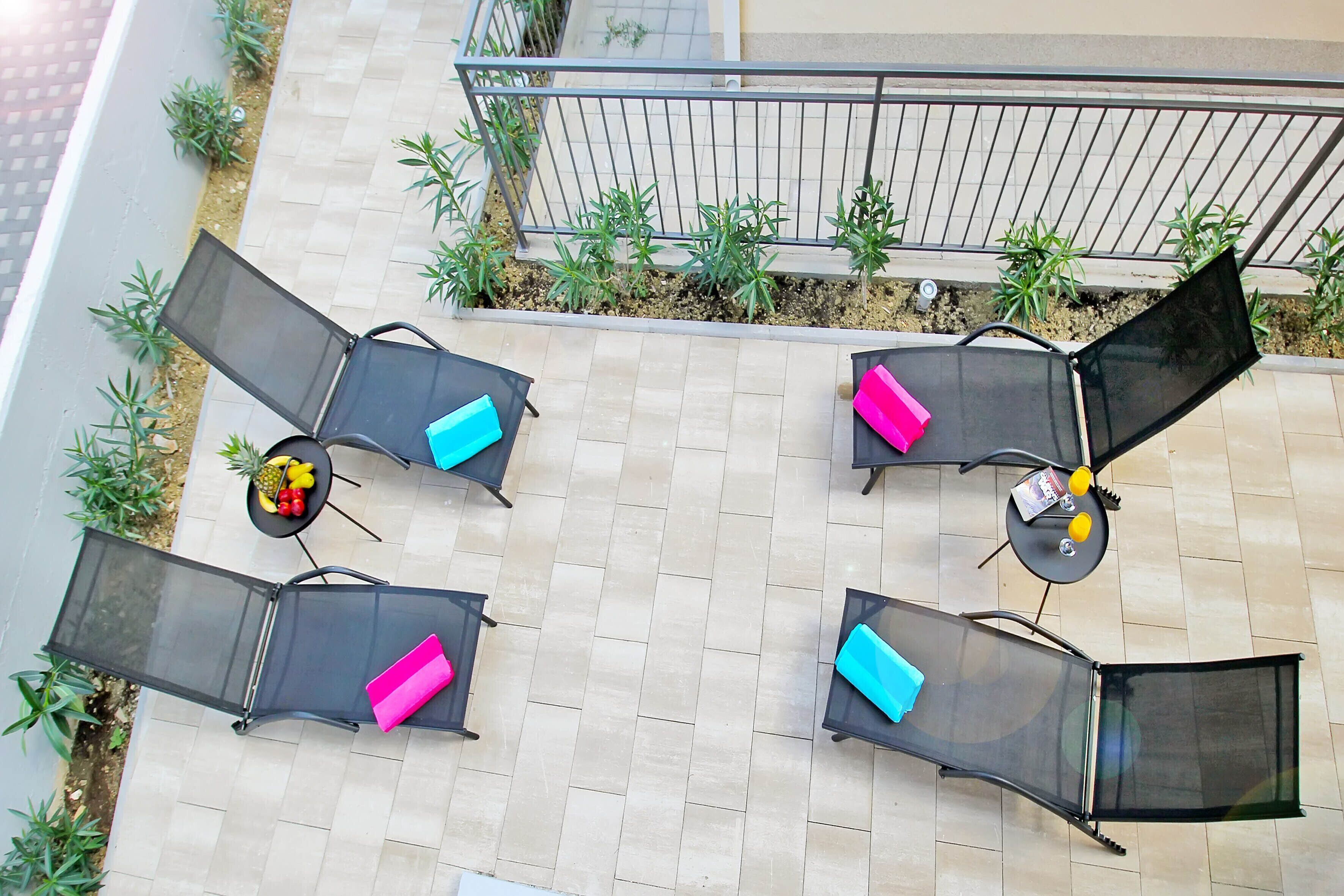 A rooftop terrace with four lounge chairs, each with a cushion, and a small table with a fruit bowl and a book.
