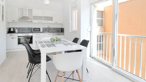 A modern kitchen with white cabinets, a dining table with chairs, and a large sliding glass door to a balcony. - Bacan Family Apartments (Konavle)