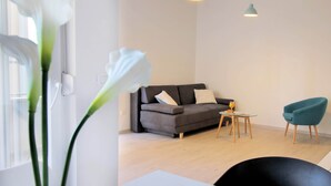 A modern living room with a grey sofa, teal armchair, and a small round table with a glass top. - Bacan Family Apartments (Konavle)