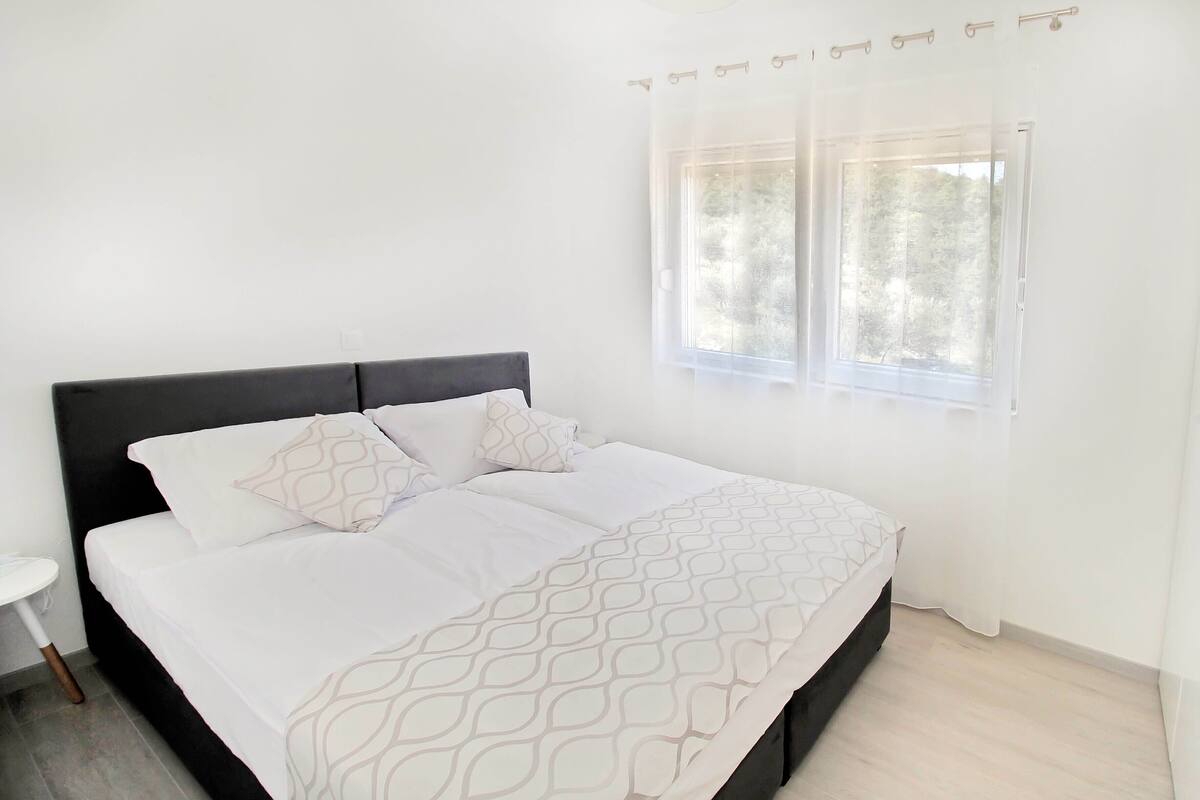 Un dormitorio con cama, mesita de noche y ventana con cortinas.
