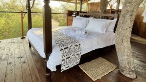 A wooden four-poster bed with white linens and a patterned throw, set in a rustic room with a wooden floor and ceiling beams. - Ondudu Safari Lodge (Omaruru)