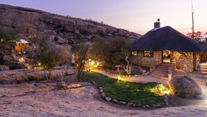 A stone house with a thatched roof, surrounded by a landscaped garden with pathways and outdoor lighting. - Ondudu Safari Lodge (Omaruru)