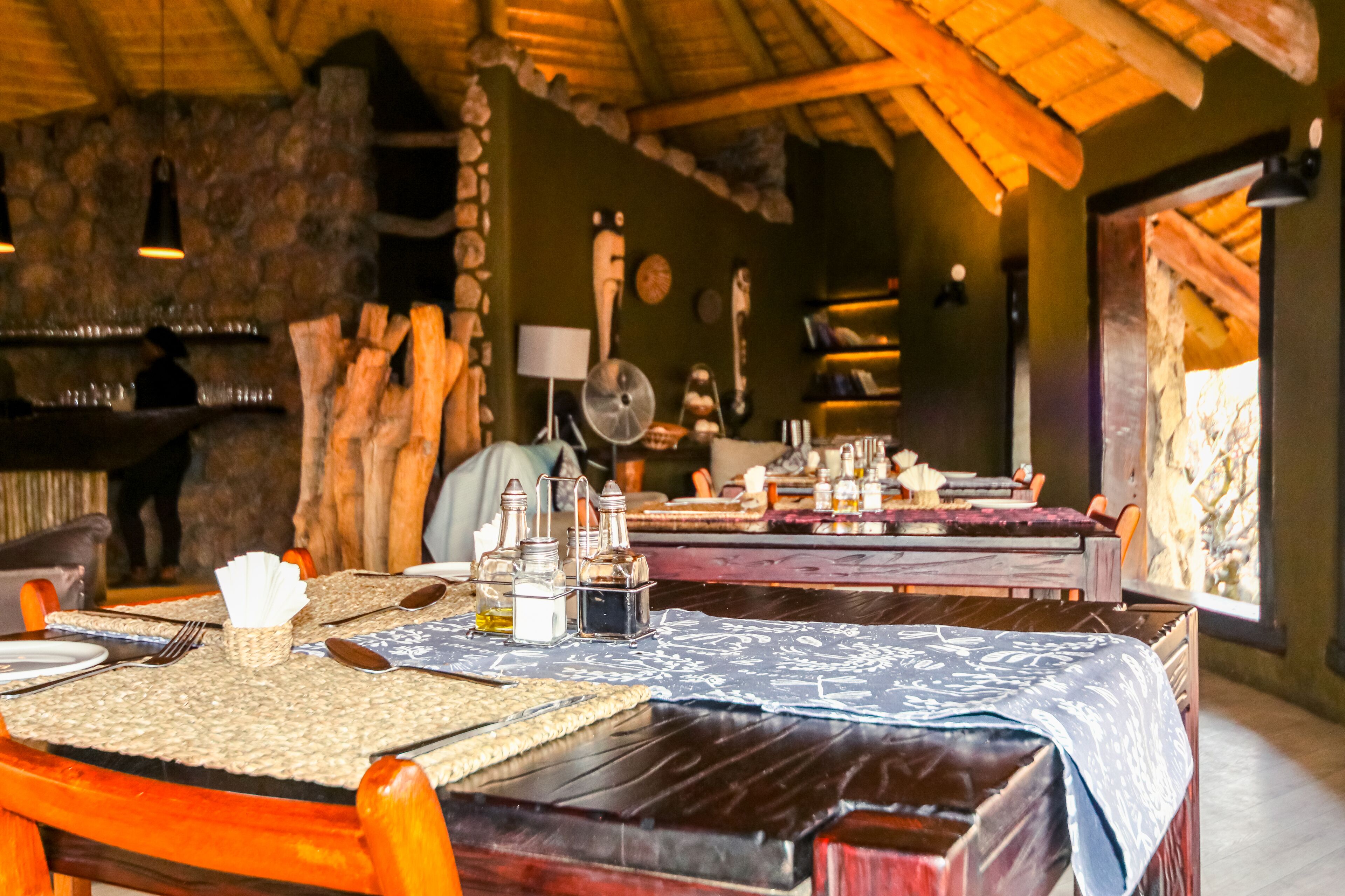 Un coin repas rustique avec des tables et des chaises en bois, des murs en pierre et un toit de chaume.