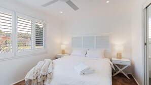 A bedroom with a bed, two bedside tables, a ceiling fan, and a window with blinds. - 81 Horace St - Wifi, Pool and air conditioning (Shoal Bay)