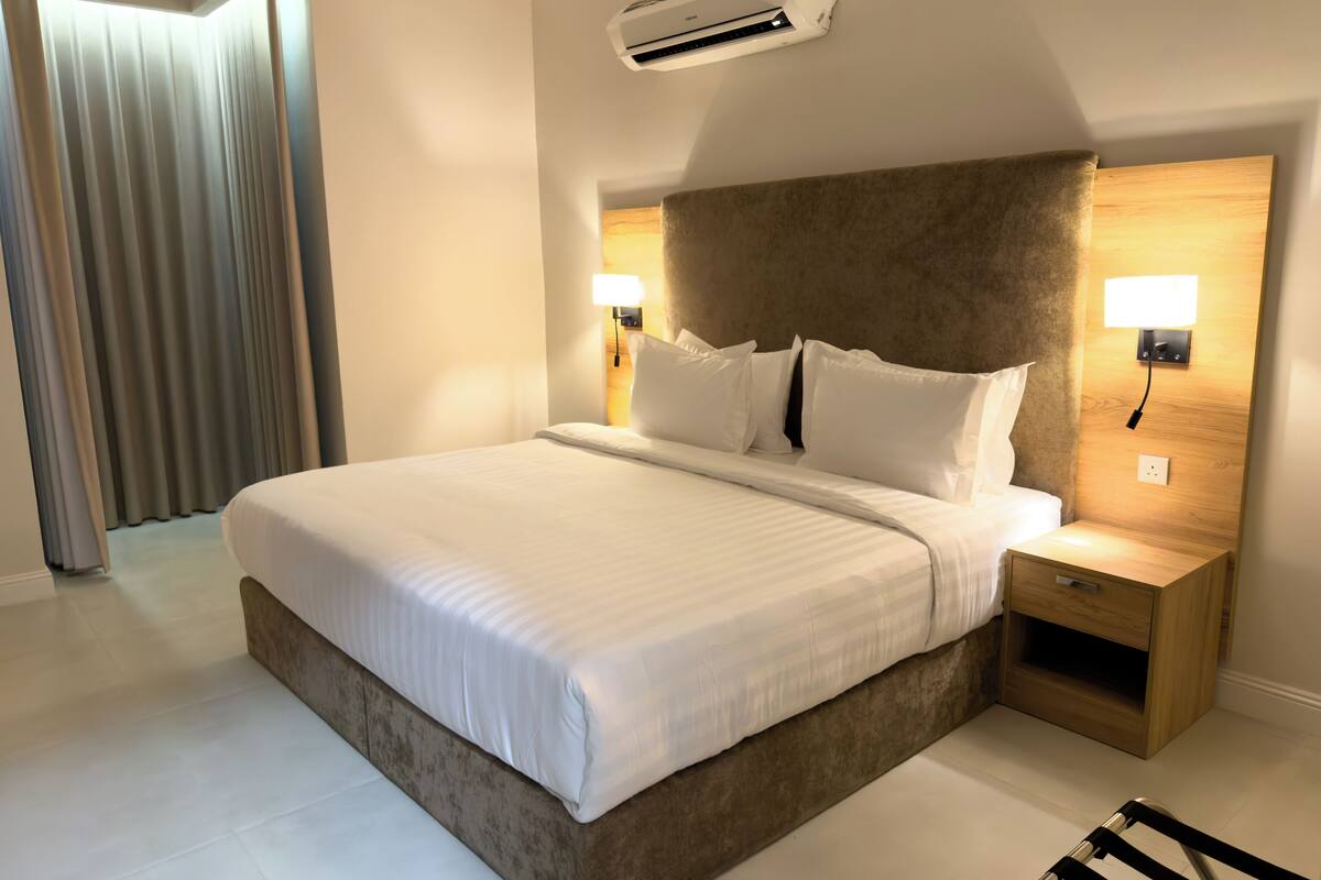 Una habitación de hotel moderna con una cama grande, dos lámparas de noche, un equipo de aire acondicionado y una mesita de noche de madera.