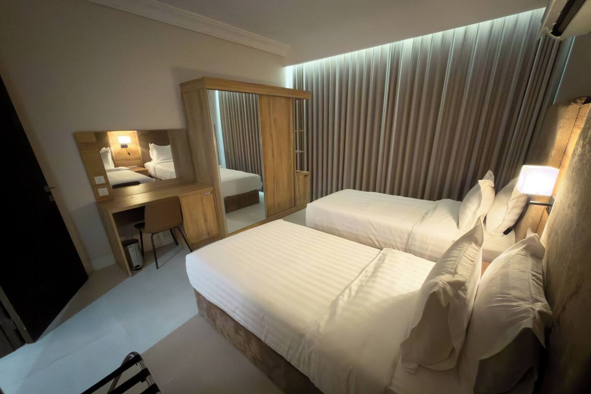Habitación de hotel con cama, escritorio, silla, armario y espejo.