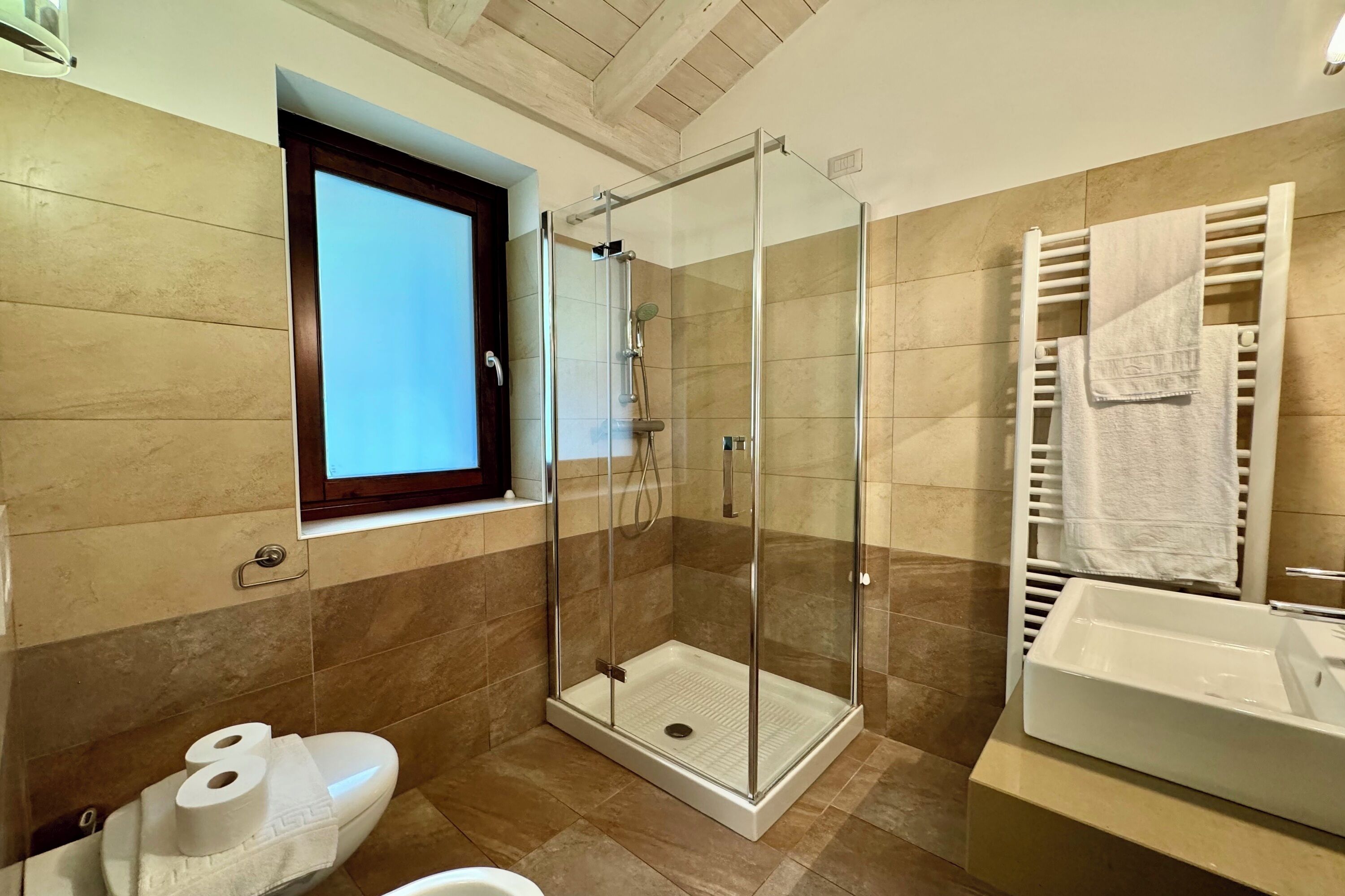A bathroom with a glass-enclosed shower, a toilet with a towel, and a sink.