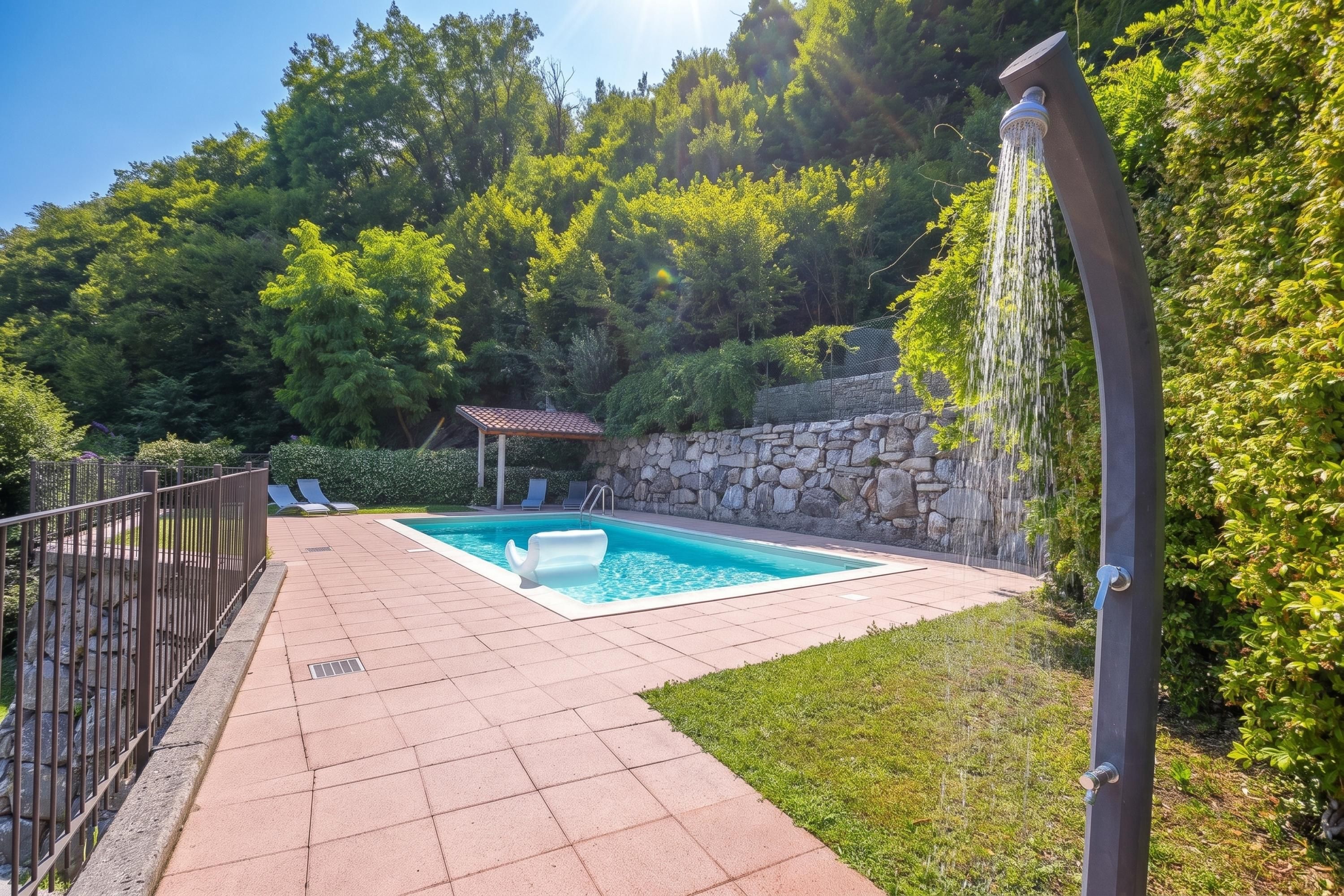 Una piscina con muretto in pietra e una piccola area coperta, immersa nel verde.