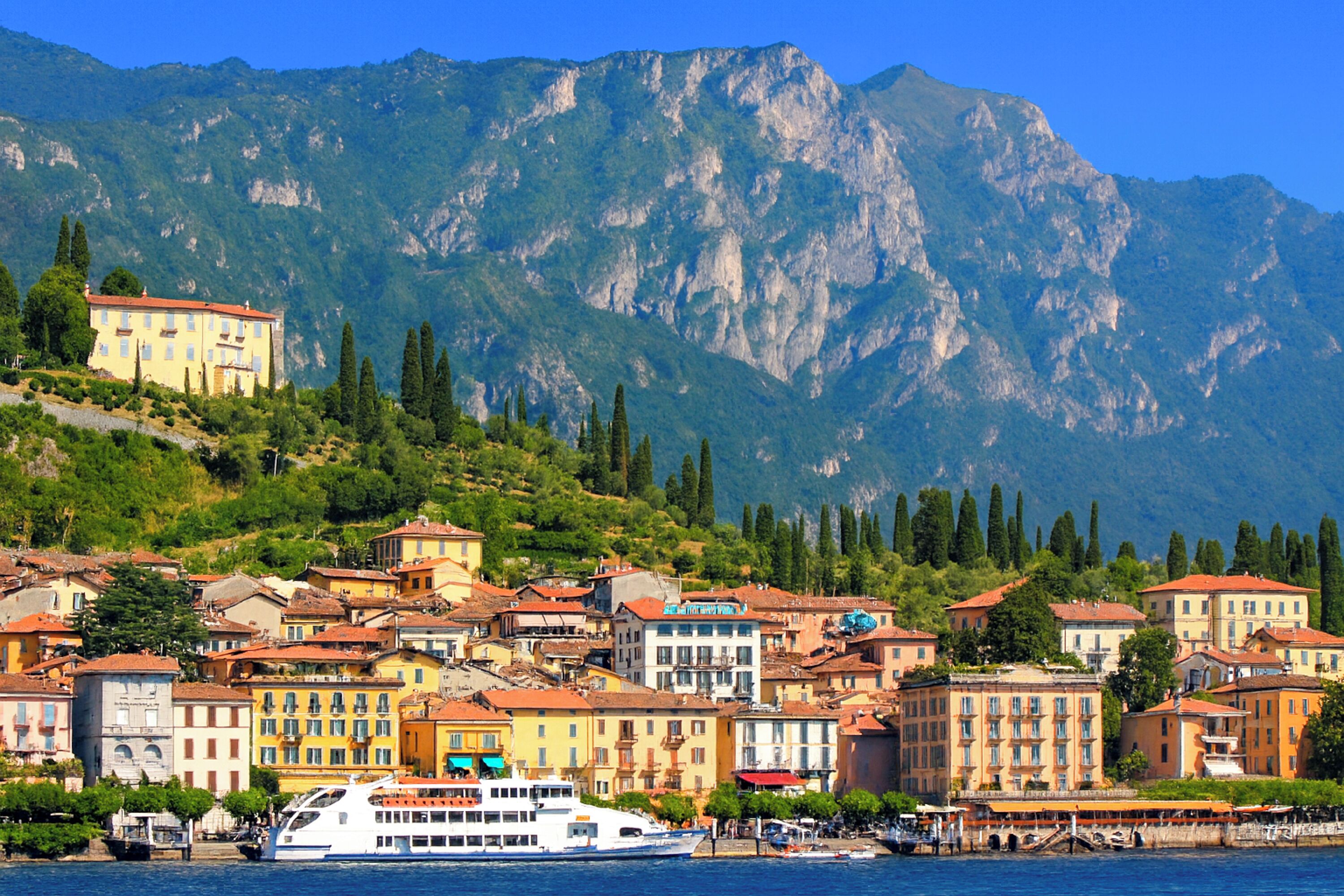 A coastal town with historic buildings, a waterfront, and mountains in the background.