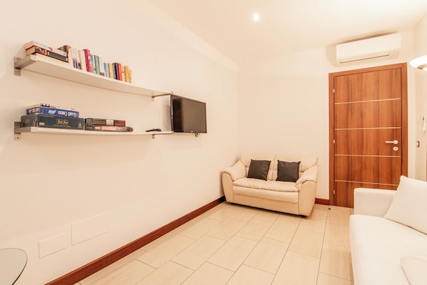A living room with a sofa, a TV mounted on the wall, and a wooden door.