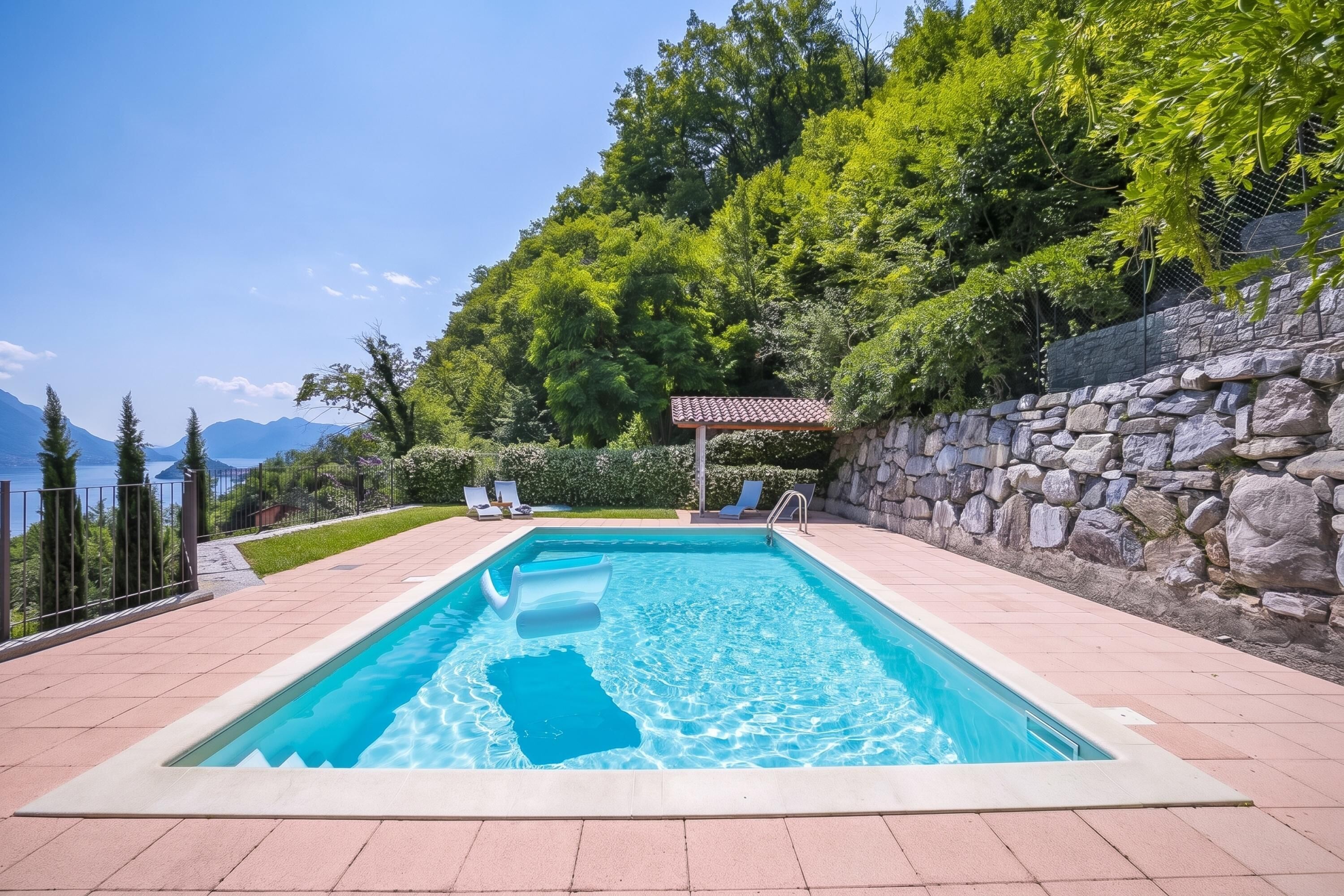 A rectangular swimming pool with clear blue water, surrounded by a stone wall and a tiled deck.