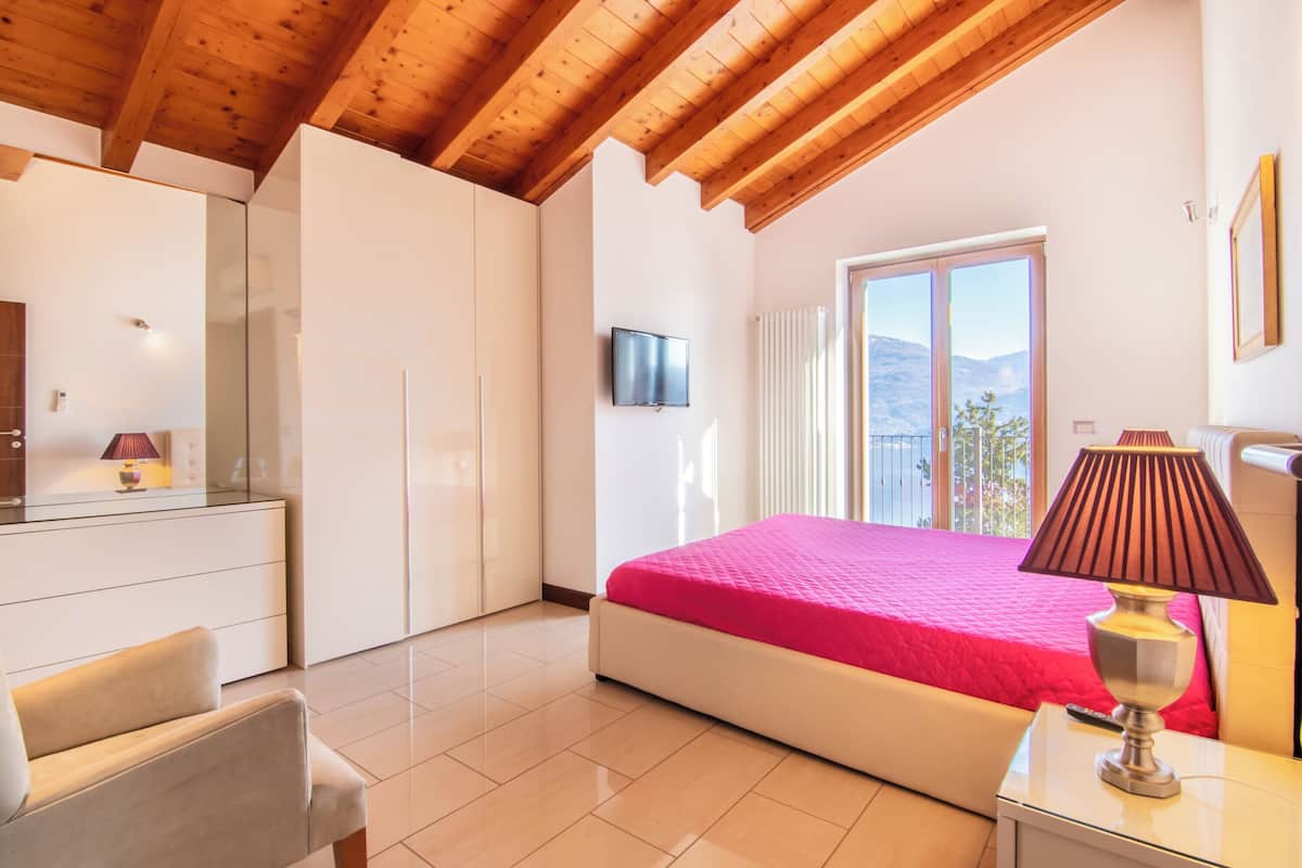 A bedroom with a bed, a TV, a lamp, and a view of the outdoors.