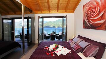 A bedroom with a large bed, a balcony with a view of the sea, and a painting of a rose on the wall.