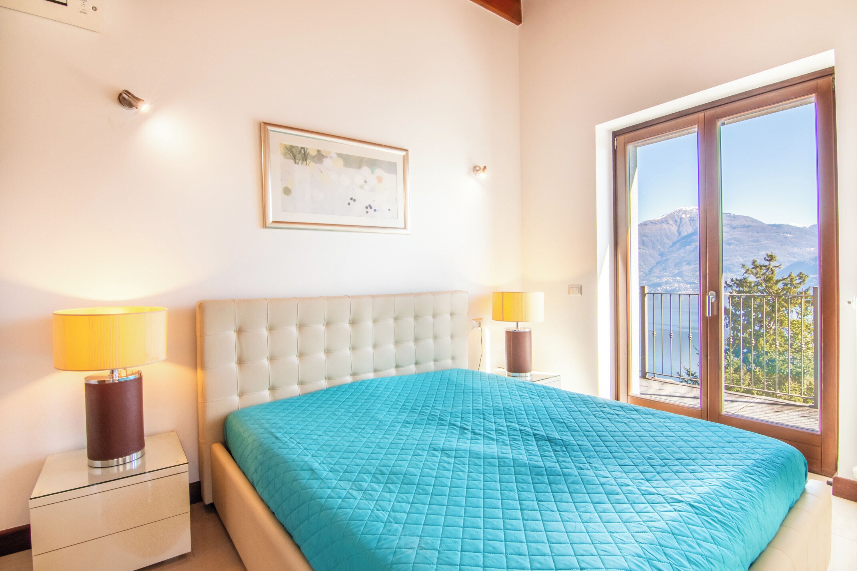 A bedroom with a large bed, a window with a view of mountains, and a framed picture on the wall.