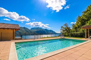 Una piscina con vista a la montaña, un deck con cerramiento y un edificio con techo de tejas.