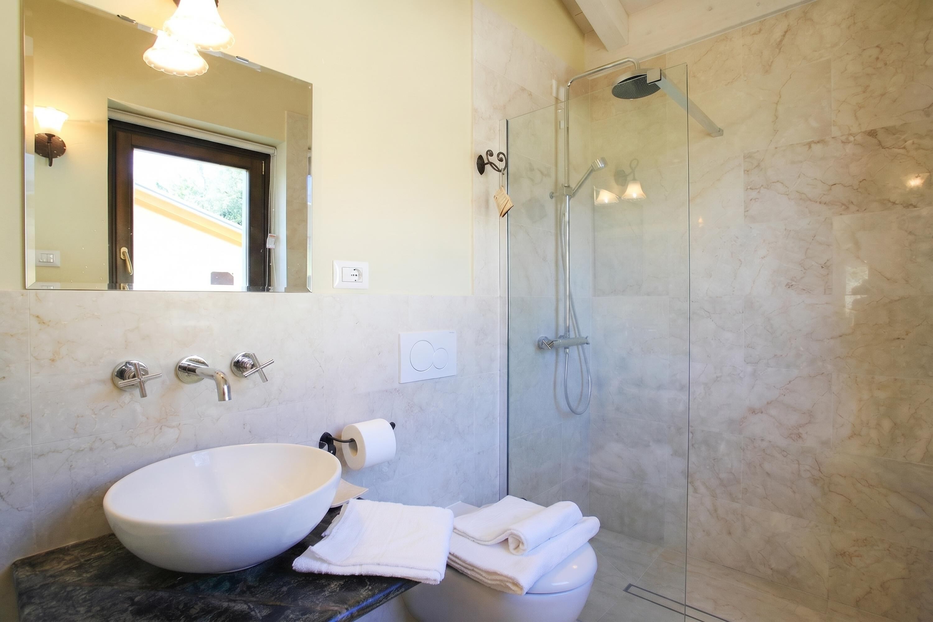A bathroom with a large white sink, a toilet, a glass-enclosed shower, and a mirror above the sink.