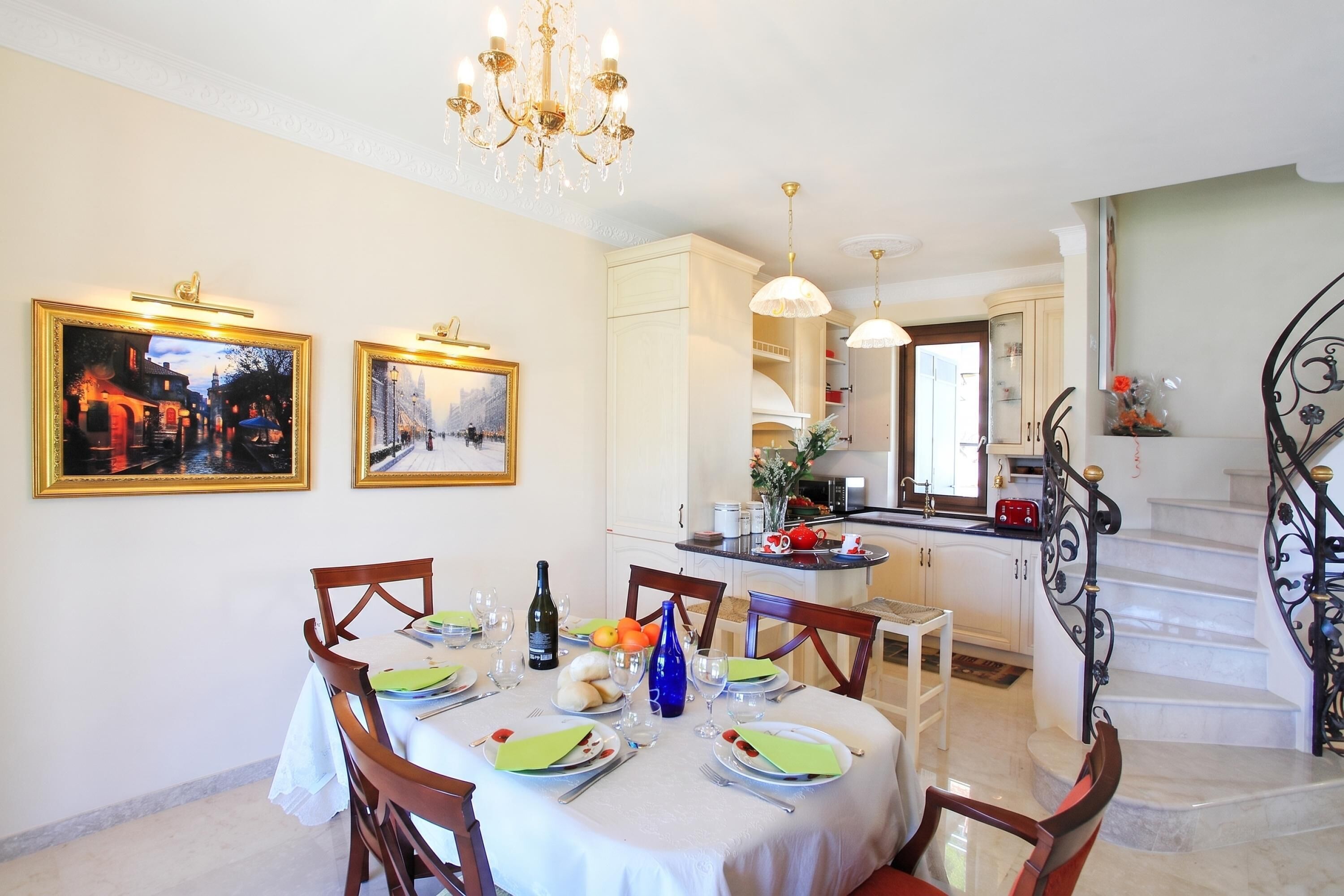 Un coin repas avec une table dressée pour quatre personnes, un lustre et deux tableaux encadrés accrochés au mur.