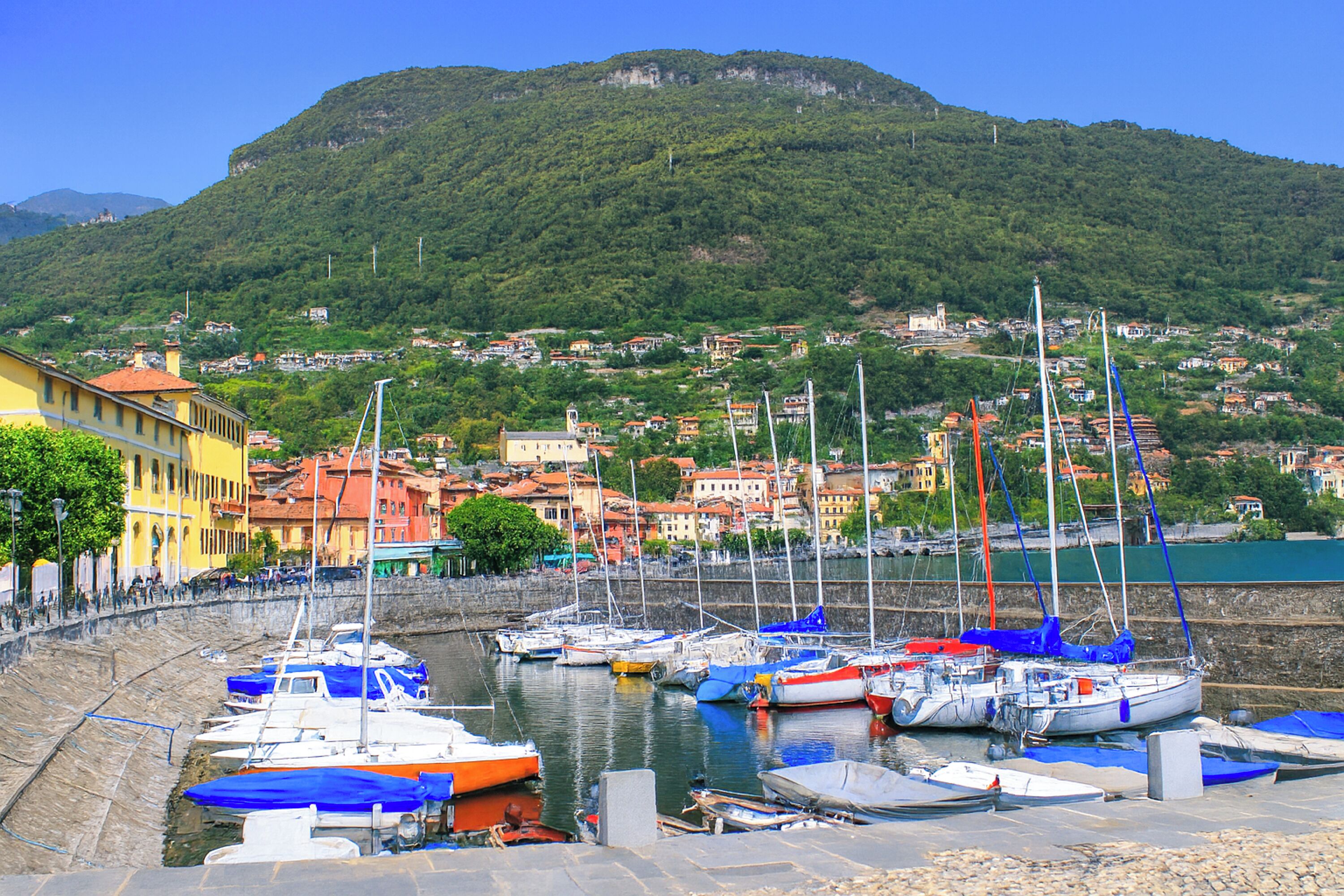 A harbor with boats docked, a stone wall, and buildings in the background.