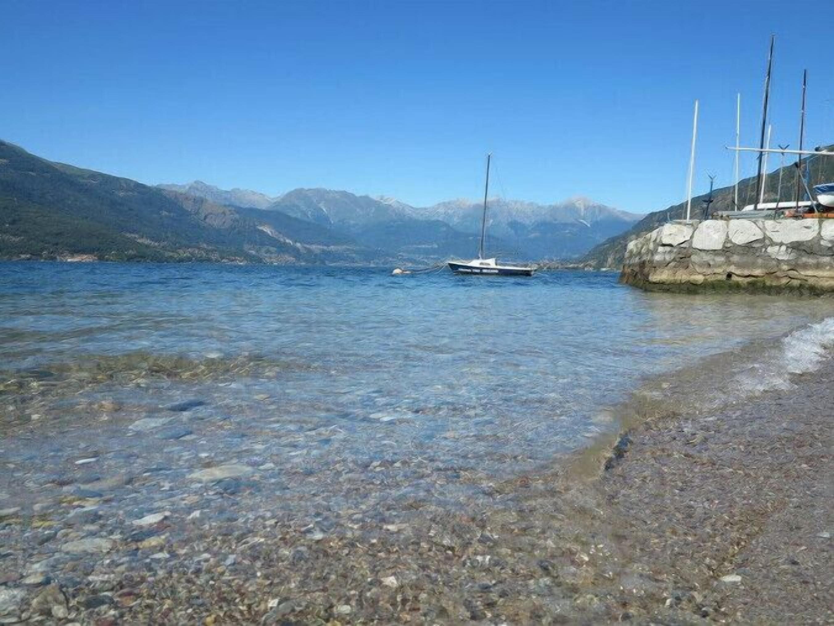 Un lago transparente con un barco amarrado a la derecha y montañas al fondo.