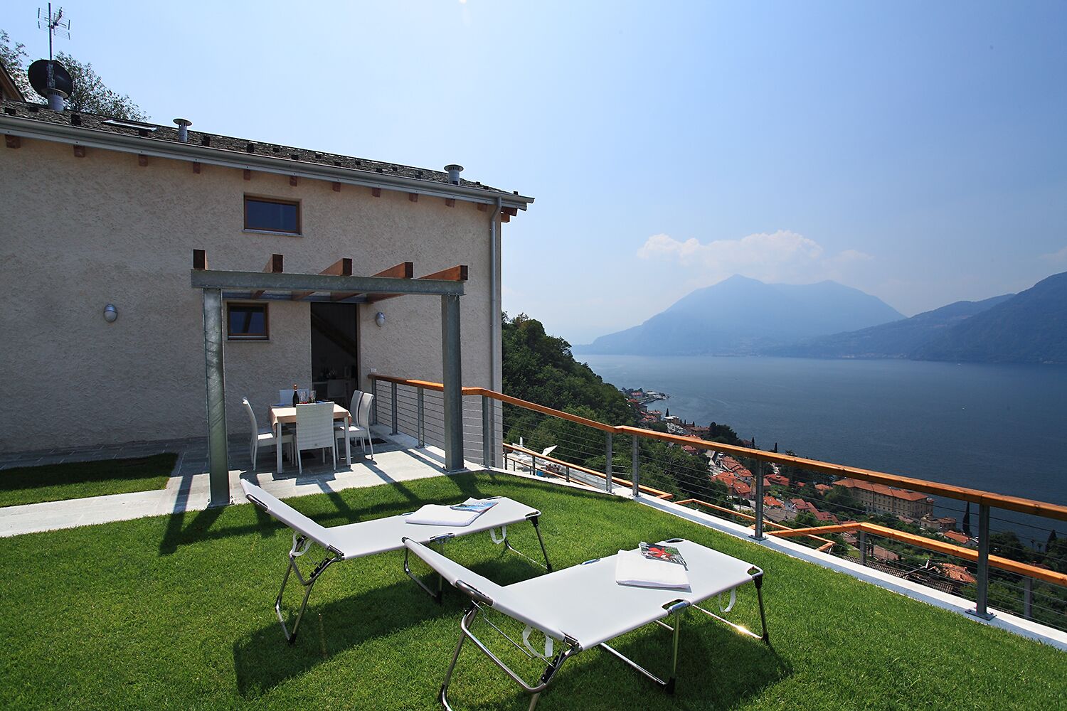 A terrace with outdoor furniture, a pergola, and a view of a lake and mountains.