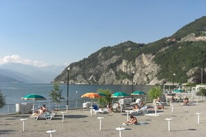 A beach with sun loungers and umbrellas, a rocky hillside in the background, and a body of water.