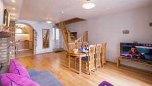 A spacious living area with a wooden dining table, chairs, a sofa, a TV, and a staircase leading to an upper level. - Nobiallo Fantastico (Menaggio)